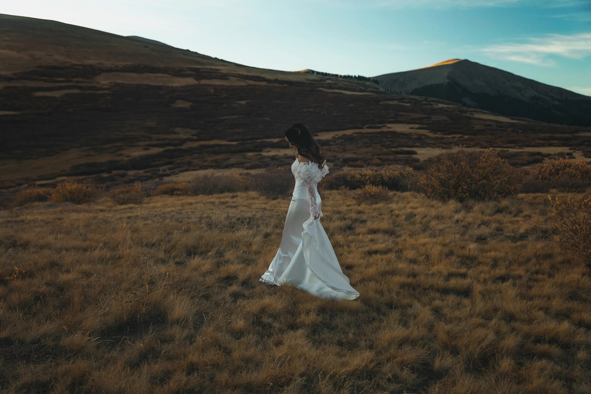 Bride in a white dress standing in a field with mountains in the background