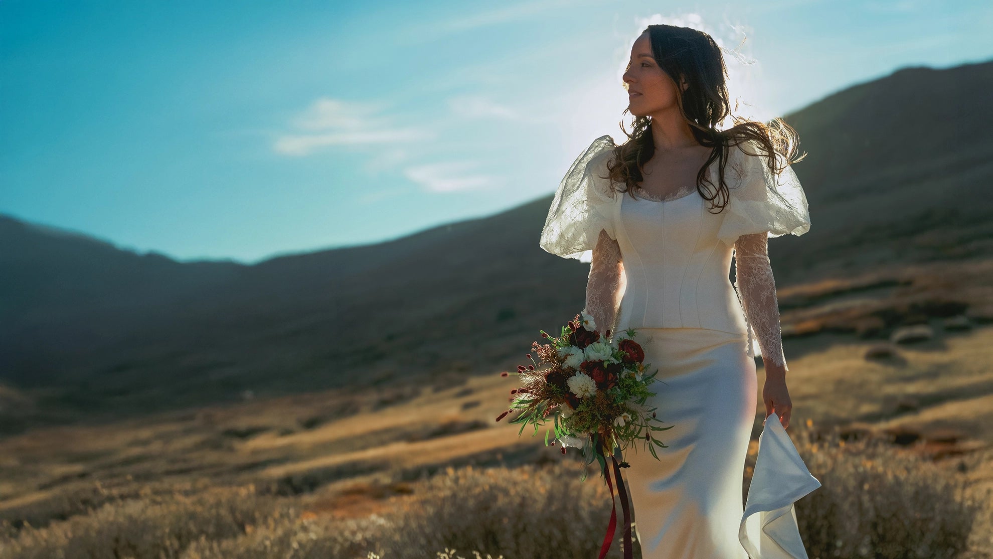 bride in a white wedding dress bridal set holding a bouquet in a desert landscape with mountains.
