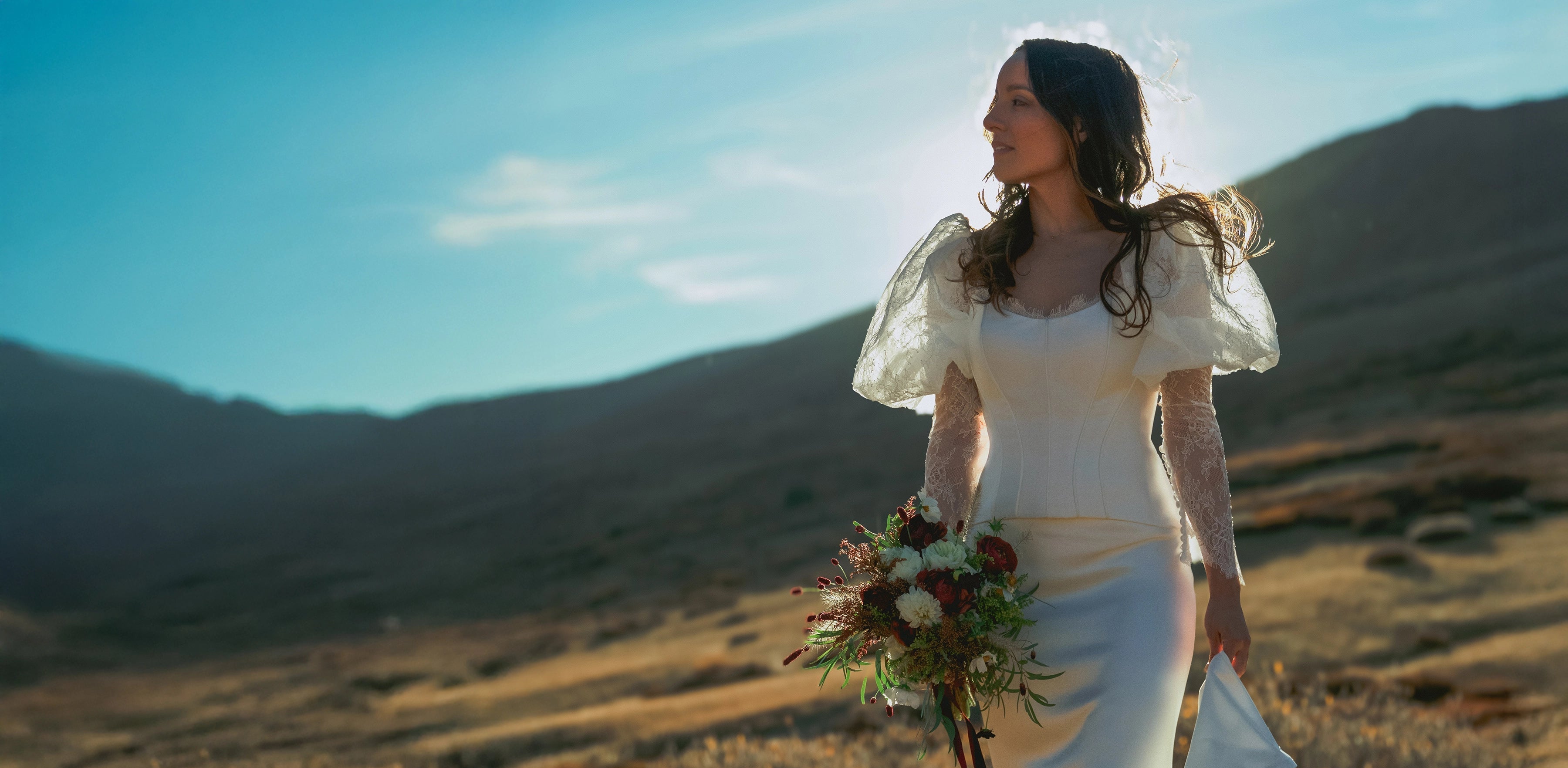 bride in a white wedding dress bridal set holding a bouquet in a desert landscape with mountains.