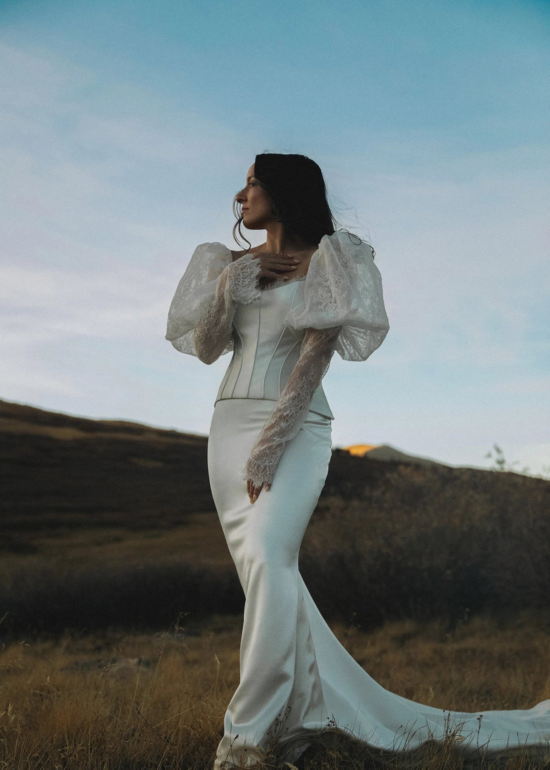 Bride in a white wedding dress standing in a field with a blue sky.