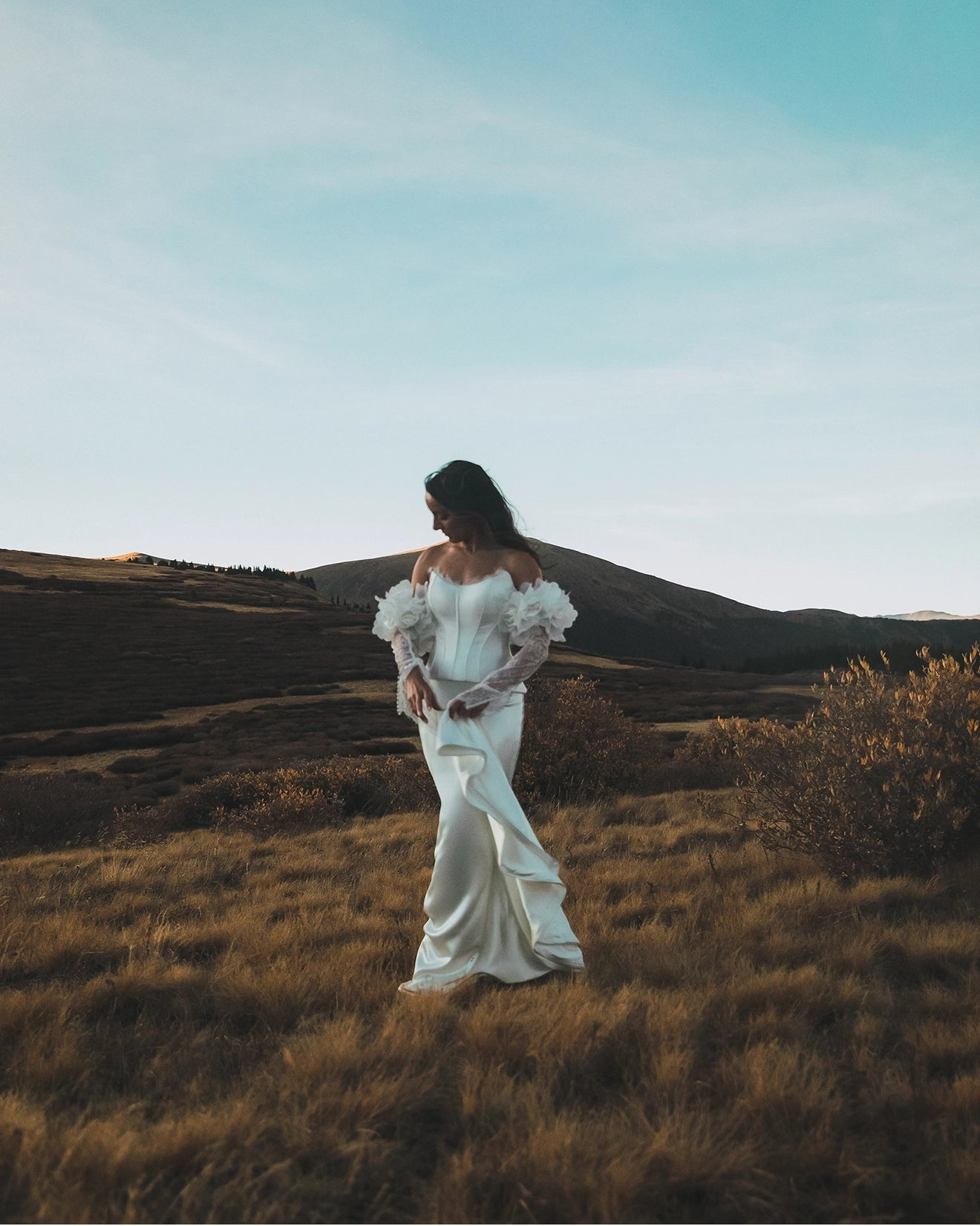 Woman in a white wedding dress standing in a field with mountains in the background