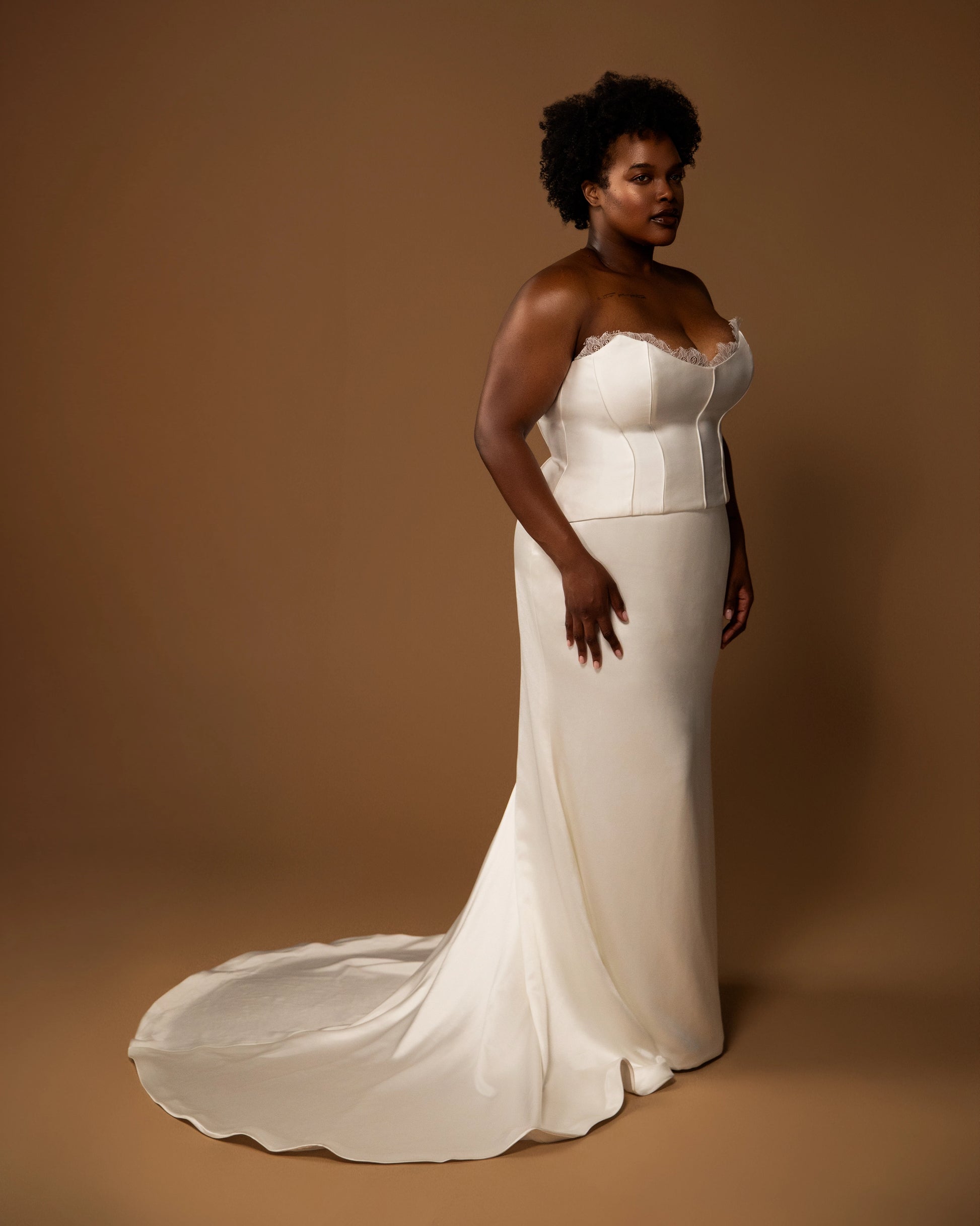 Plus size bride wearing a white wedding dress bridal set against a brown background