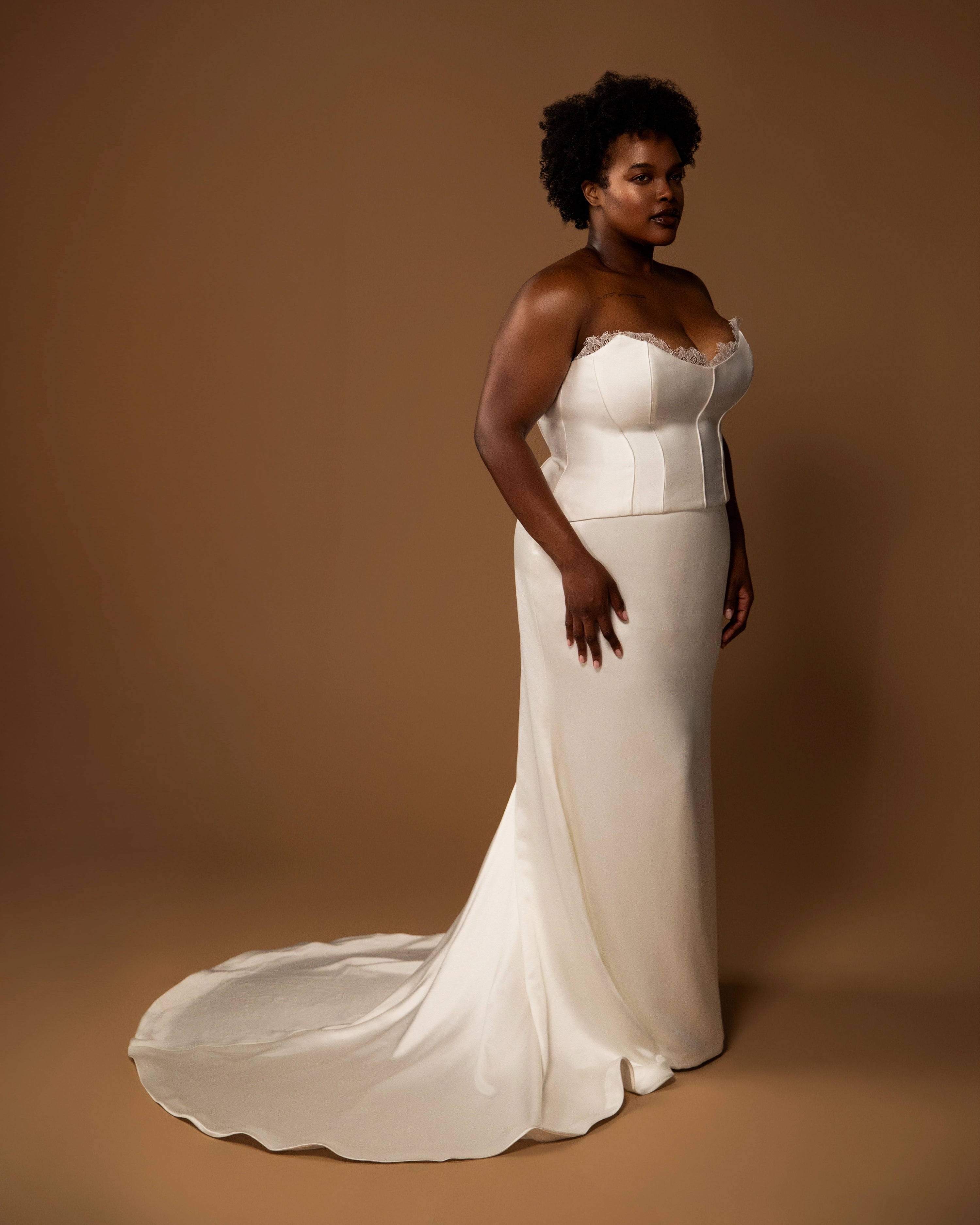 Plus size bride wearing a white wedding dress bridal set against a brown background