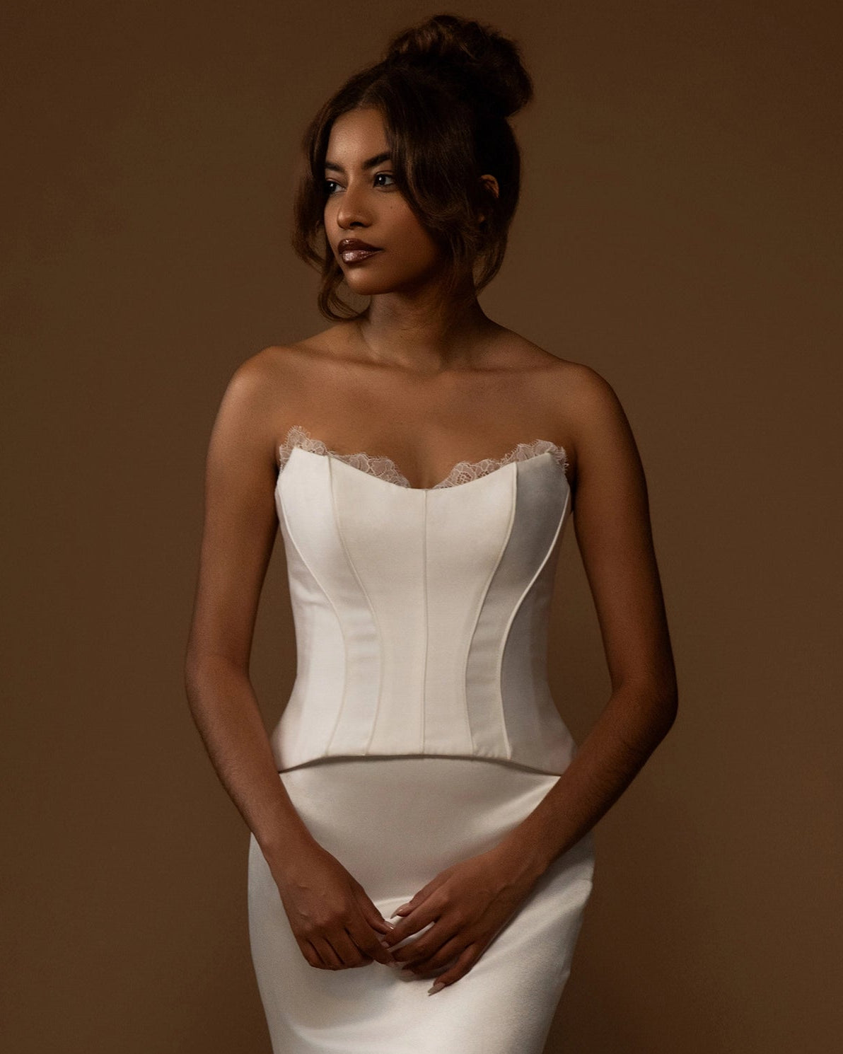 Woman wearing a white strapless corset top and skirt against a brown background
