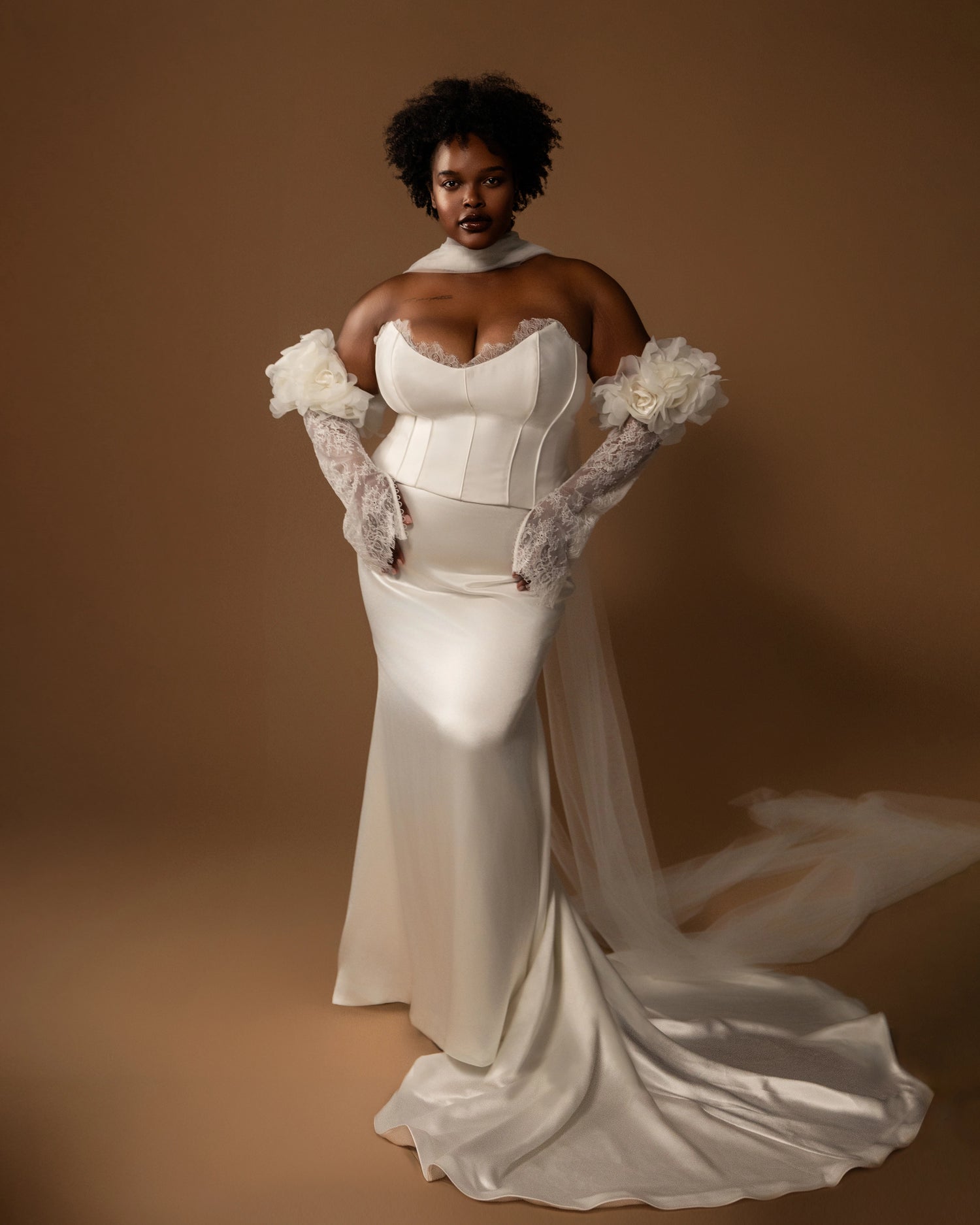 Plus size bride in a off white wedding dress set with lace gloves against a brown background