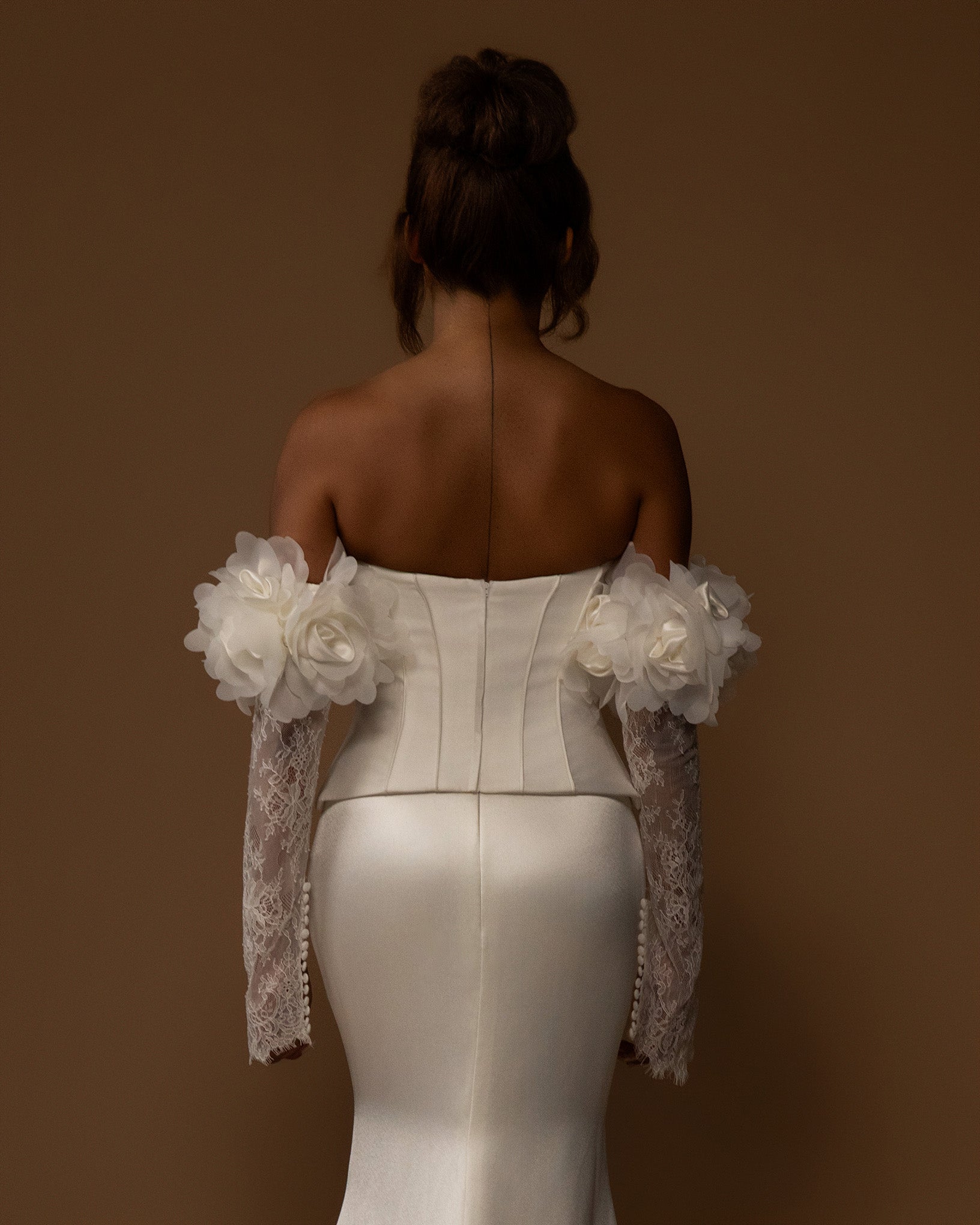 White wedding dress with floral shoulder accessories on a brown background