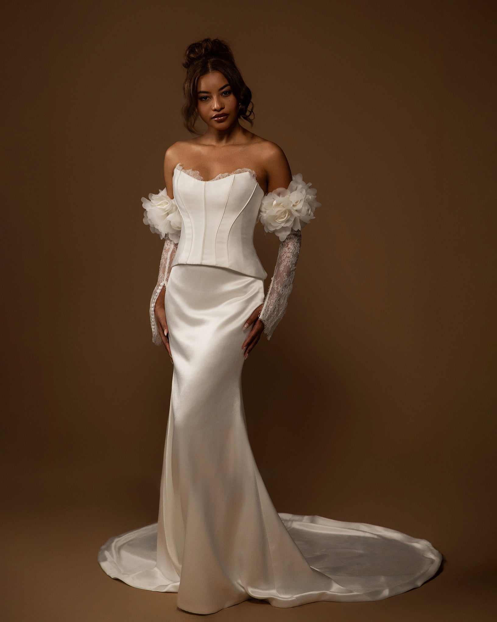 Woman wearing a white wedding dress with floral sleeves against a brown background