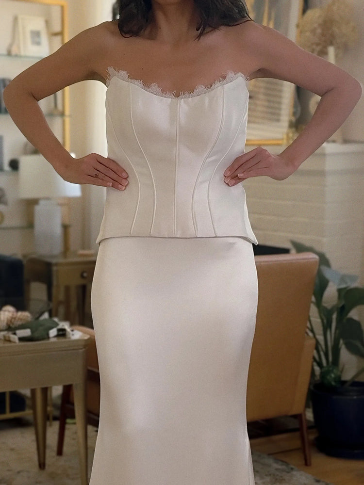 White strapless gown with lace detailing on a blurred indoor background